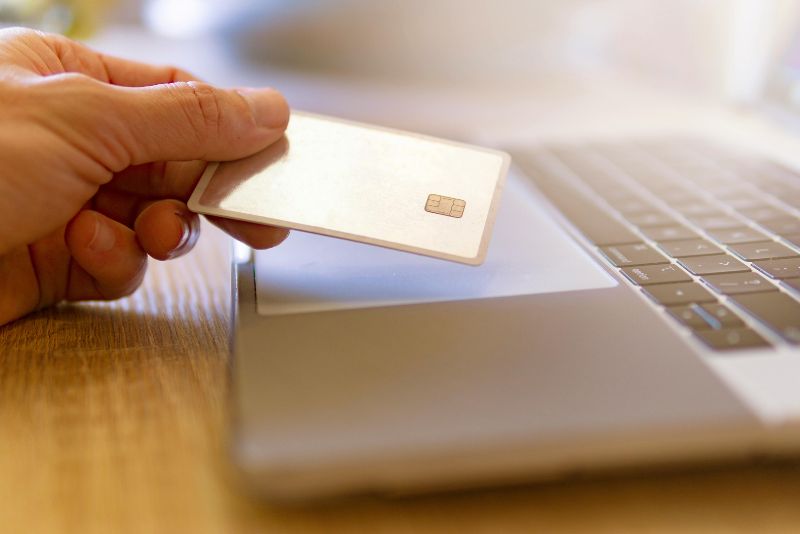 Osoba trzymająca kartę kredytową nad touchpadem otwartego laptopa, sugeruje chęć zapłacenia za odprawę celną towaru.
