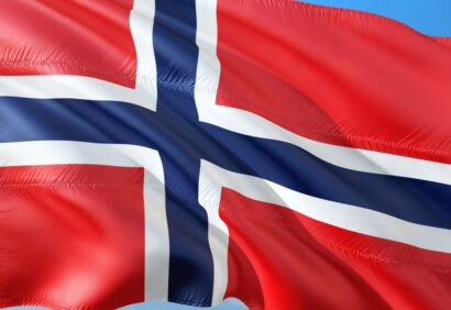 Eksport-do-norwegii Obraz przedstawia flagę Norwegii, która ma czerwone tło z niebieskim krzyżem obrysowanym na biało, falującym na tle czystego, błękitnego nieba.